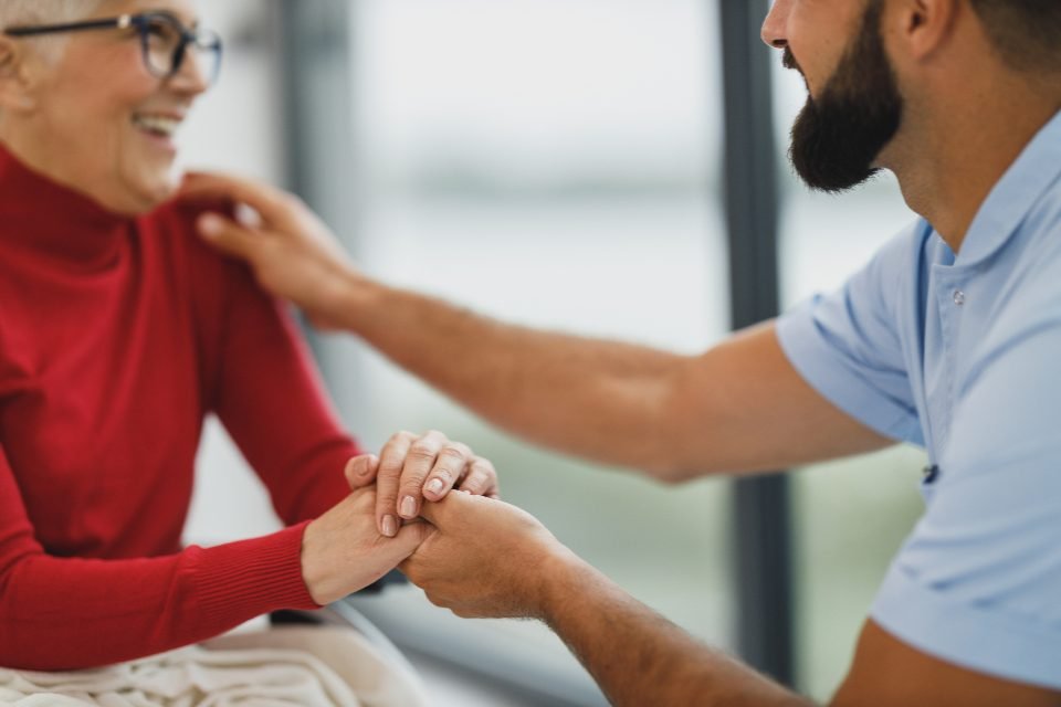 A caregiver sitting with a resident, holding her hand