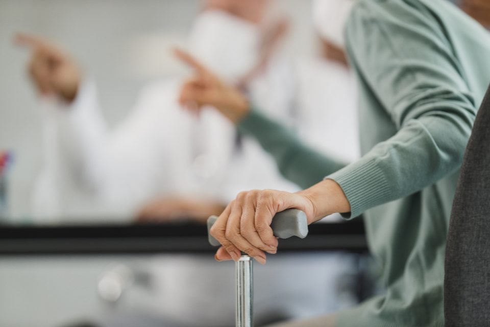 An older person’s hand resting on a walking cane